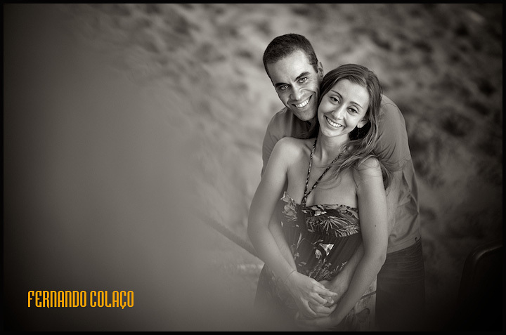 Sorrindo felizes, o noivo e a noiva em frente do areal da praia das Avencas na Parede, Cascais.