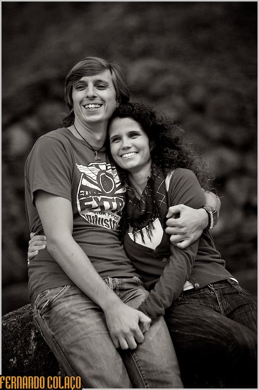 Os noivos sentados num rochedo e a rir muito.