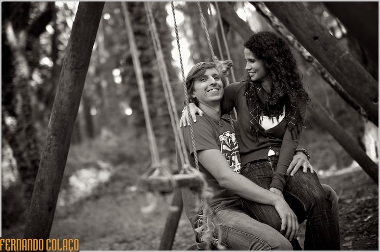 Sentada ao colo do noivo, num baloiço na parque da Peninha, a noiva olha para ele.