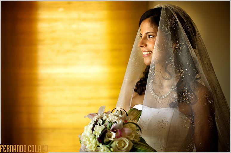 Retrato da noiva, a sorrir, com a bouquet na mão.