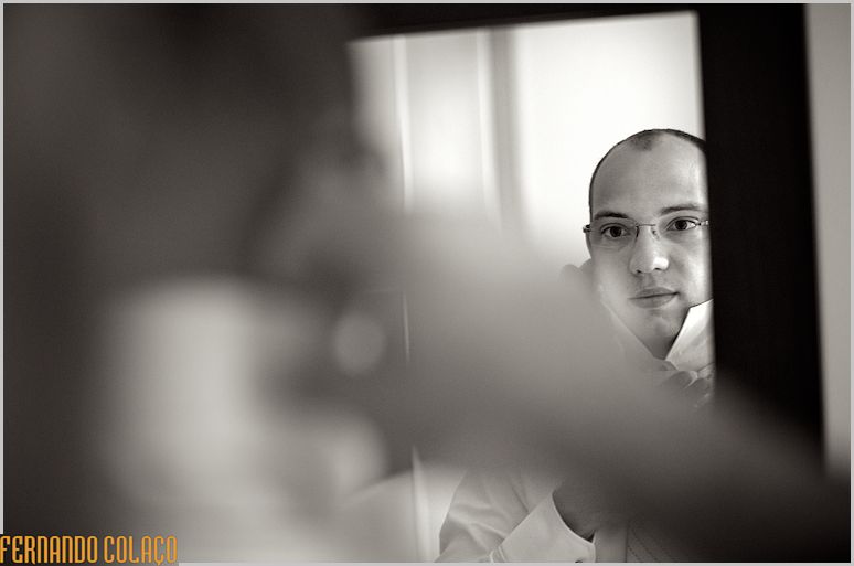In the mirror, the groom tightens his shirt collar.