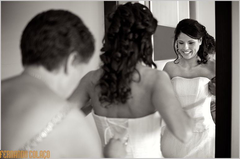 In a mirror, the bride putting on her dress with the help of her mother.