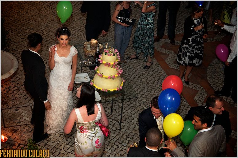 No lugar do corte do bolo, os noivo no meio dos convidados.