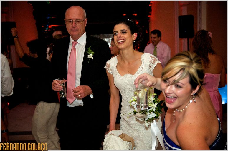A noiva, no meio de dois convidados, leva o bouquet na mão.