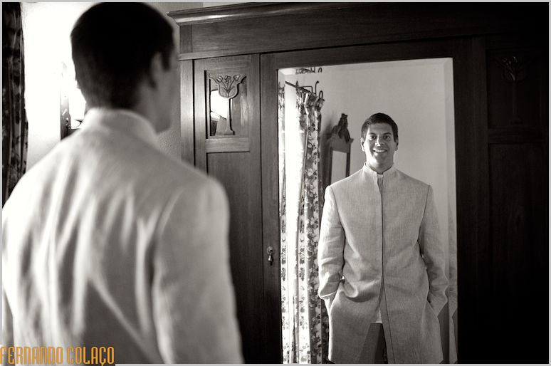 Noivo, no espelho de um móvel, olha-se quando pronto.