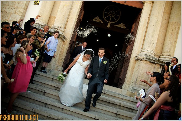 Sob nuvens de grãos de arroz, os noivos descem a escadaria da igreja.