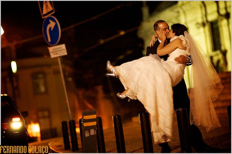 Noiva ao colo do noivo numa rua de Lisboa, à noite.
