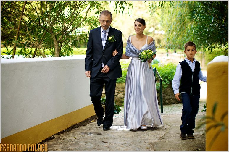 A noiva, o pai e o irmão mais novo caminha na direcção da cerimónia do casamento.