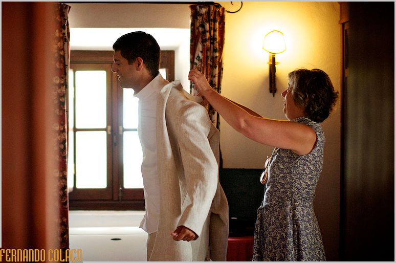 The groom's mother helping him put on his coat.