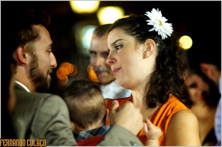 Groom talks to a friend with a baby in her arms and a flower in her hair.