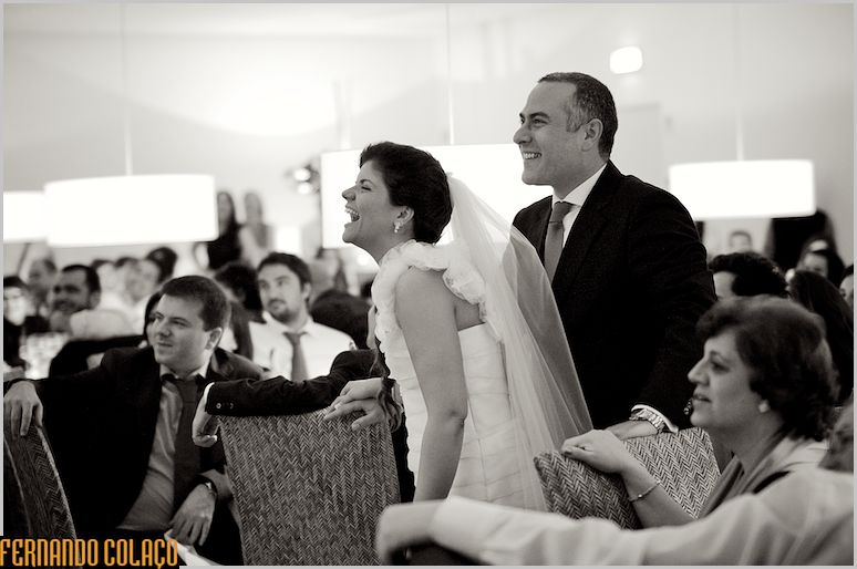 The bride and groom, in the midst of the guests, laugh at something they are seeing.