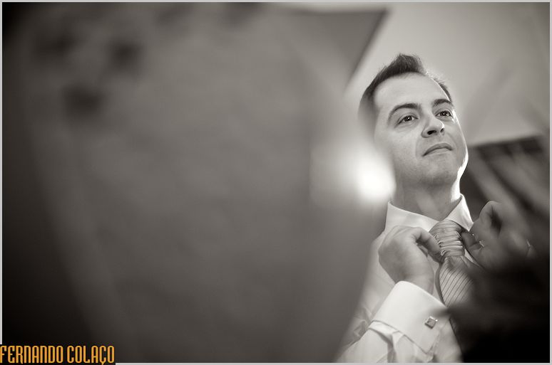 The groom adjusts the knot of his tie in the mirror.