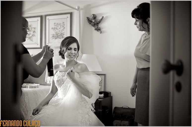 Already dressed and next to her mother, the hairdresser applies a little hairspray to the bride's hair.