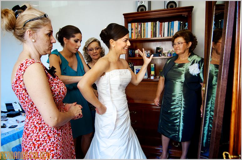 Noiva rodeada de familiares femeninos, finalizando o vestir do vestido.