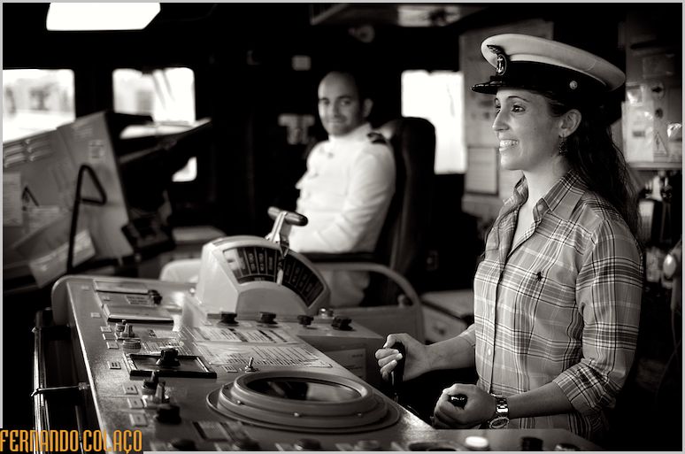 The bride pretends to steer the ship in a captain's cap, with the groom in the background.