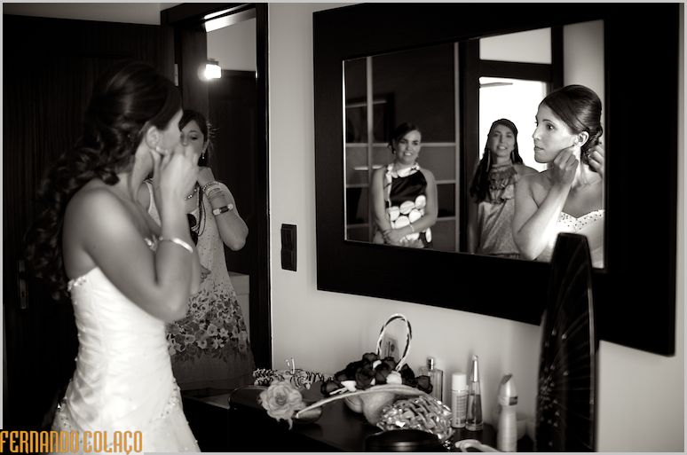 The bride putting her earrings in a mirror, with two friends.