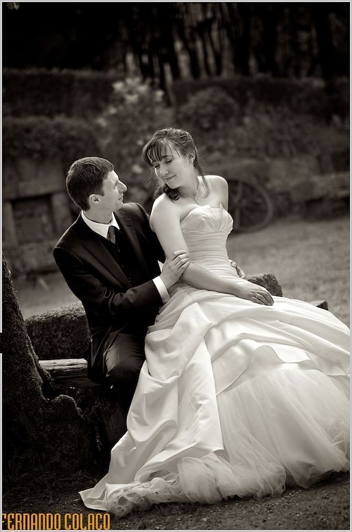 Sentado em frente do noivo, num banco do jardim, a noiva olha para trás sorrindo para o noivo.