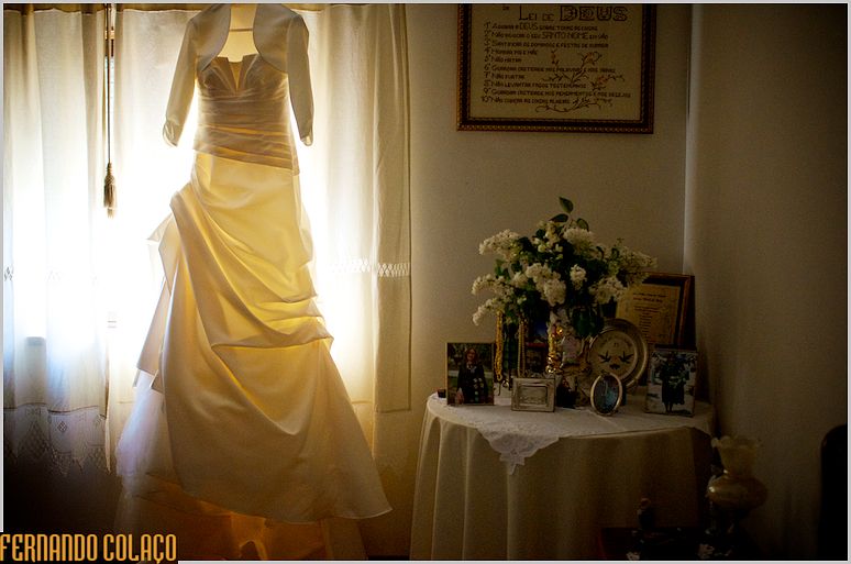 The bride's dress hung by the window, near a table decorated with photographs and flowers.