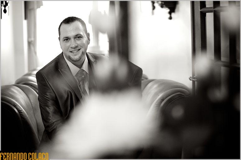 The groom, sitting on a sofa, smiling when he is ready.