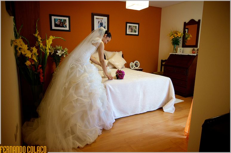 Ready to leave for the ceremony, the bride picks up the bouquet on a bed.