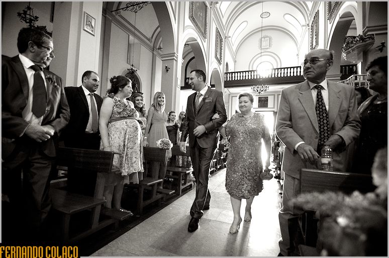 The groom, with his mother, walks through the church among the guests.