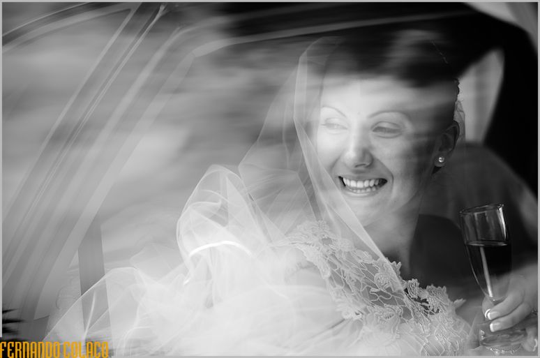 The bride smiling, view from a car window with reflections and a glass of champagne in her hand.