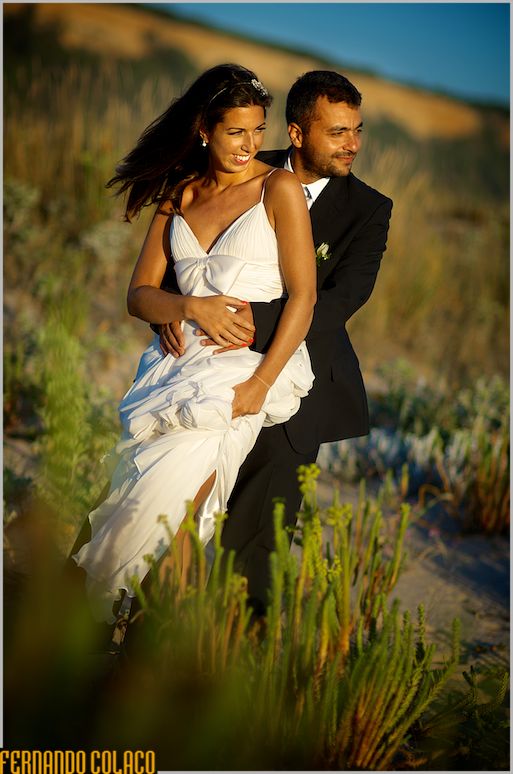 Bride and groom, standing, amidst the plants on the beach and under the light of the end of the day.