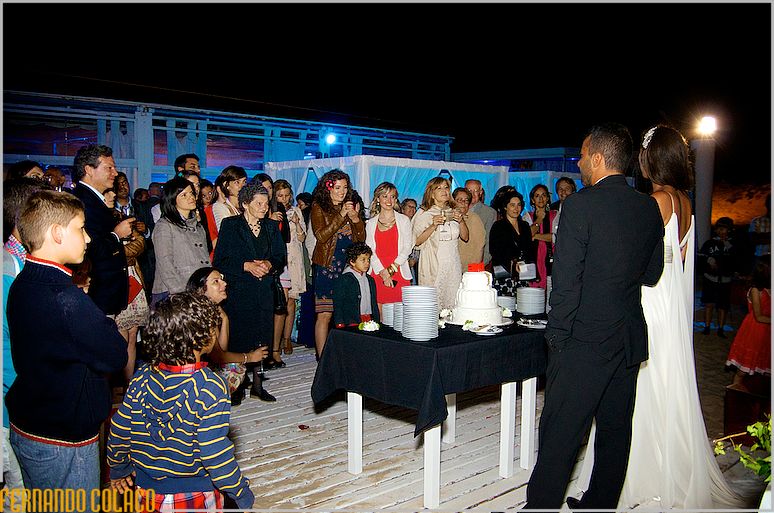 The bride and groom at the wedding cake table, in front of their guests.