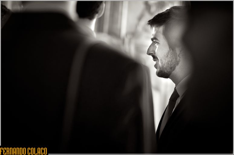Among unfocused guests, the groom in profile, listening.