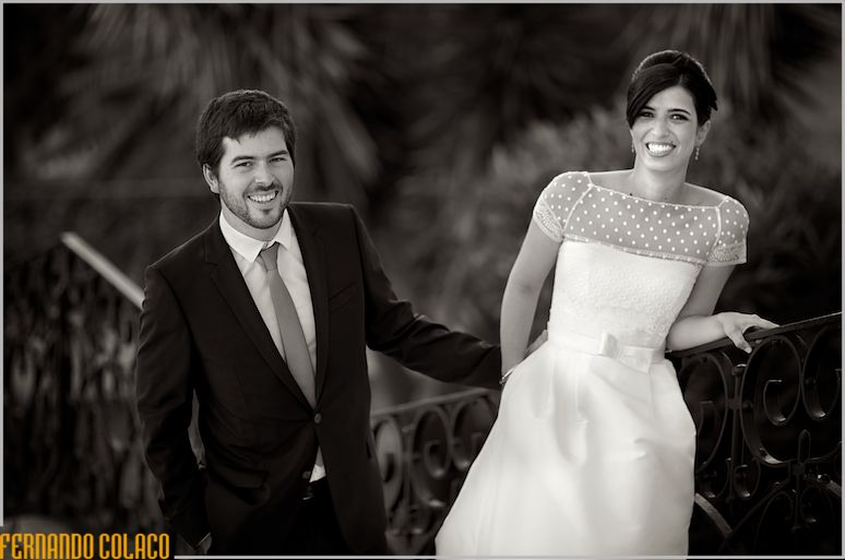 Laughing, the bride and groom by the balustrade with trees in the background.