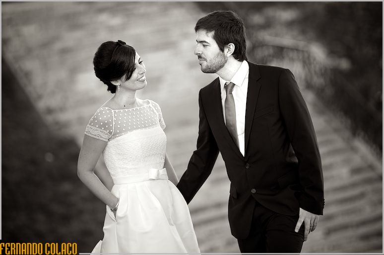 On the stairs, the groom looks at the bride, with hands in her dress pockets, next to the Palácio da Cruz Vermelha.