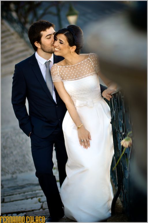 On the stairs, standing, the groom kisses the bride, who laughs with satisfaction.