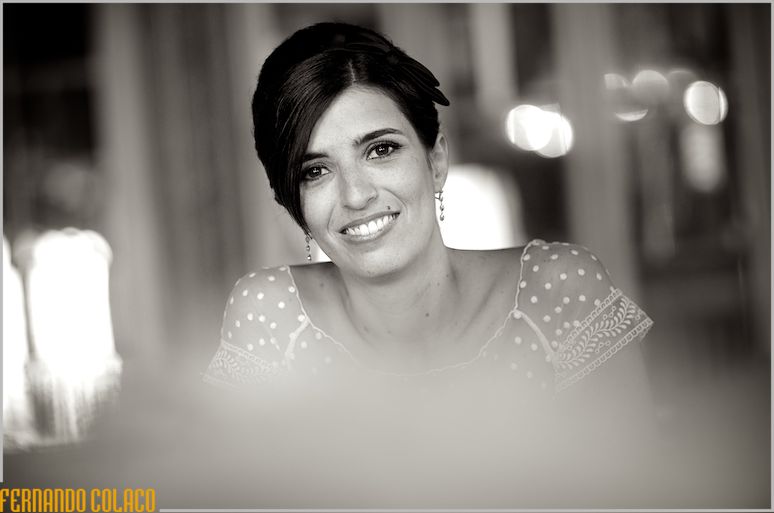 In a black and white portrait, with blurs in front, the bride smiles at the wedding photographer.