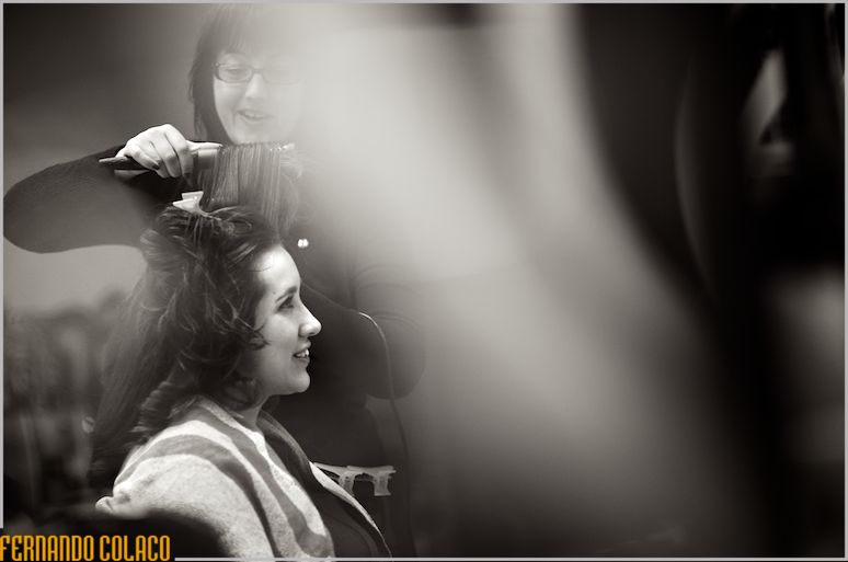 Bride, in profile, getting her hair done behind blurred objects.