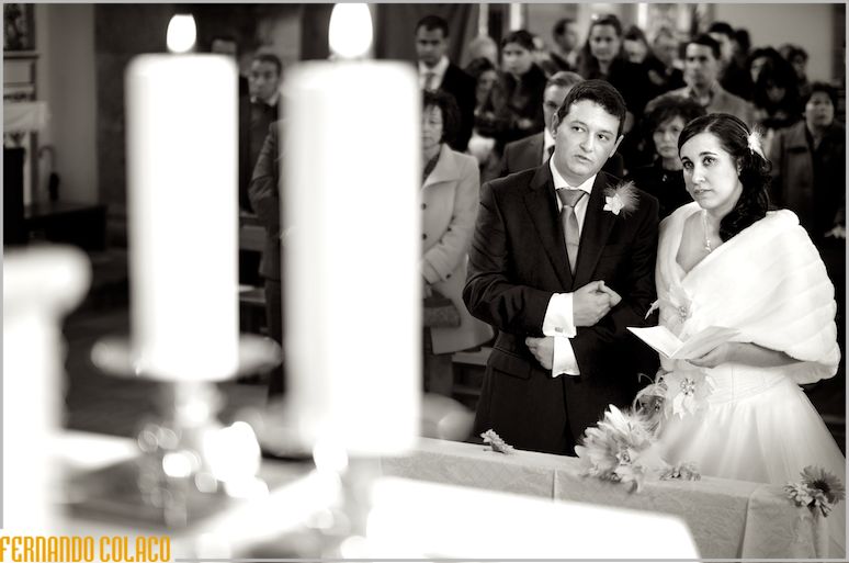 The bride and groom at the altar, between two large lit candles and the guests.