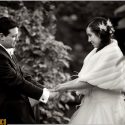 Looking at each other and holding hands, the groom and the bride with blurred trees of the Quinta da Hera in Covilhã, behind, by the wedding photographer.