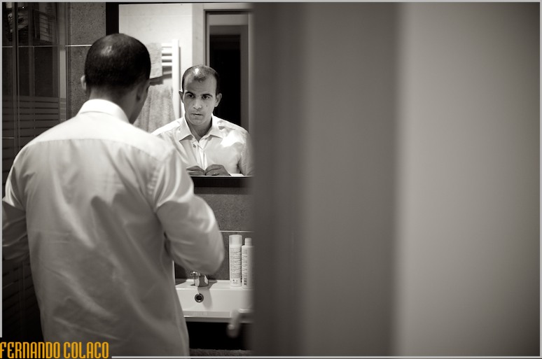 Num espelho, o noivo abotoa a camisa do fato do casamento.