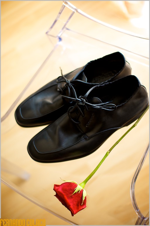 Os sapatos pretos do noivo, ao lado de uma rosa vermelha.