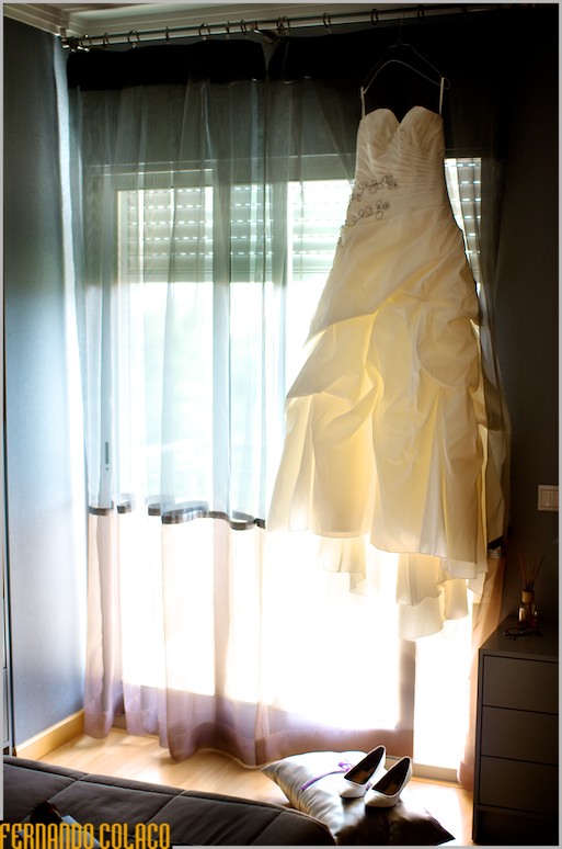 O vestido da noiva, pendurado numa janela com os sapatos por baixo.