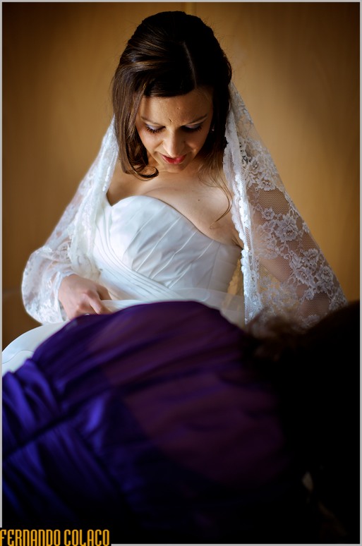 A noiva olha para baixo, enquanto a mãe acerta o vestido.