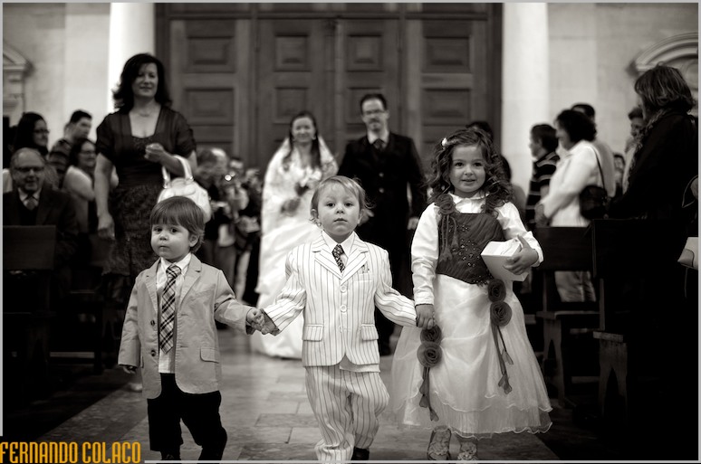 Uma menina e dois meninos caminham à frente da noiva, na igreja, para o altar.