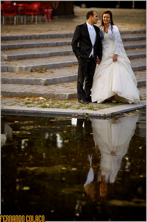 Em frente a lago num jardim, os noivos conversam.