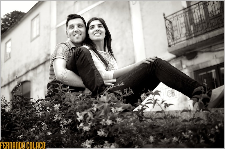 Sentados num muro com flores, a noiva encostado no noivo.