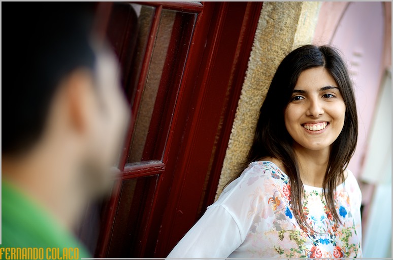 Encostada junto de uma porta em Colares, a noiva olha para o noivo, desfocado.