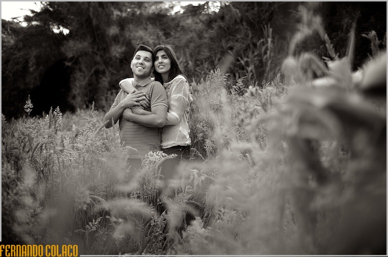 A noiva abraça o noivo por detrás e, juntos, olha para longe, dentro de um campo de flores selvagens.