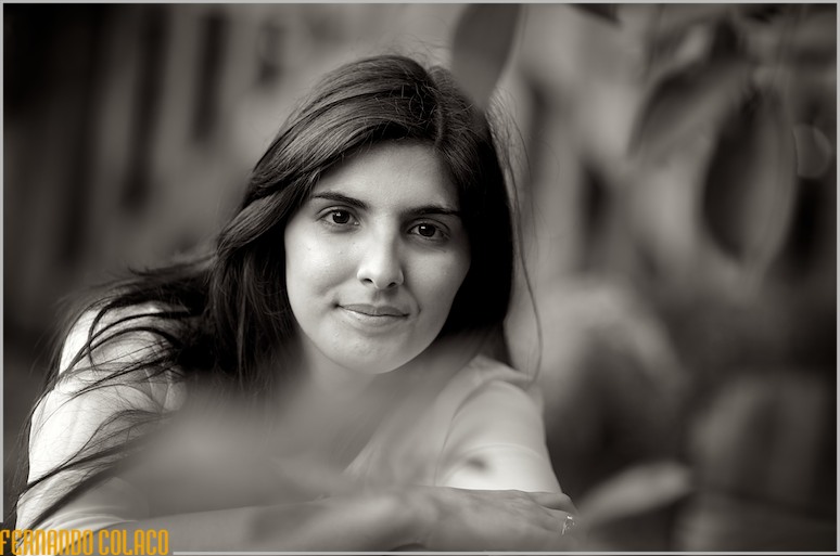 A noiva, envolta em folhagens de árvores, olha para o fotógrafo de casamento.