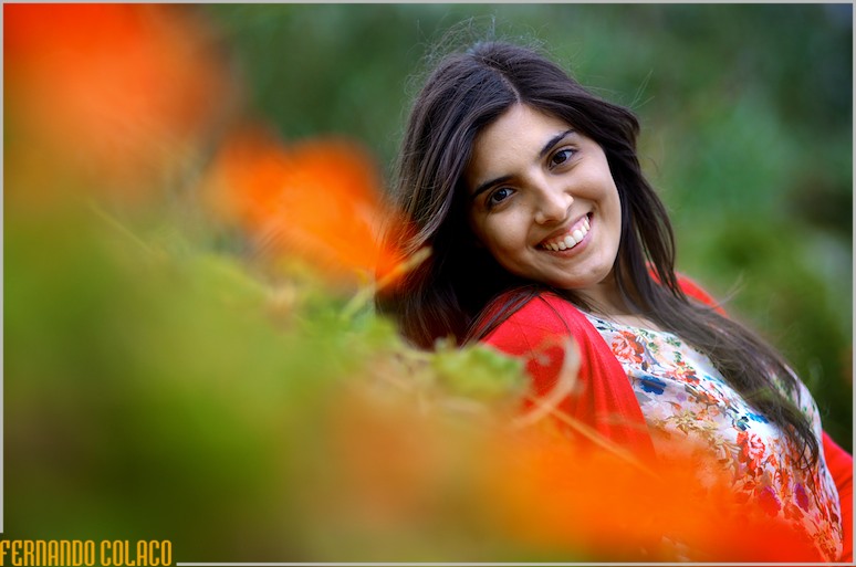 A noiva, reclinada, entre flores alaranjadas e o verde das plantas silvestres.
