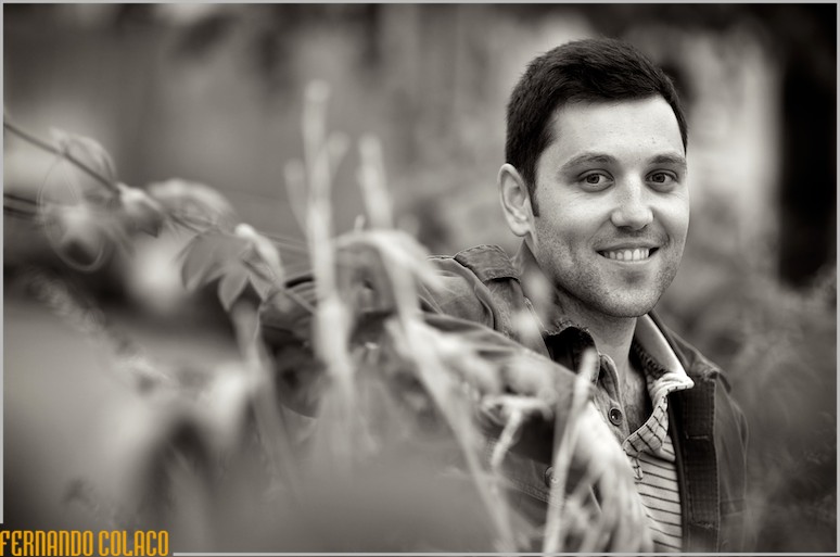 Envolto entre plantas sobre um muro, desfocadas, o noivo sorri.