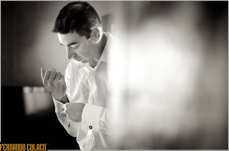 De manhãzinha, o noivo abotoa os botões do punho da camisa pra o casamento.