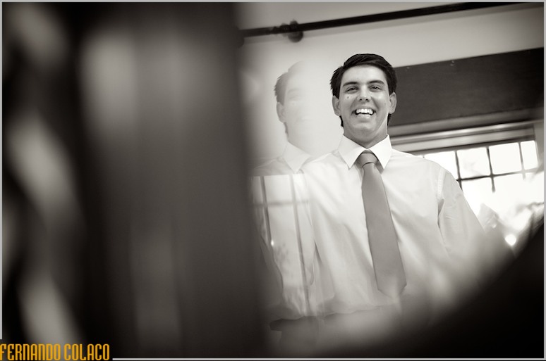 Num espelho de um móvel em casa dos pais, o noivo ri bem disposto.